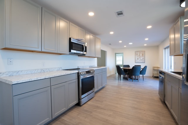 kitchen with gray cabinetry, light stone counters, stainless steel appliances, and light hardwood / wood-style floors