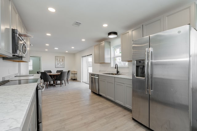 kitchen featuring gray cabinetry, sink, appliances with stainless steel finishes, light hardwood / wood-style floors, and light stone counters