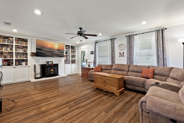 living room featuring built in features, dark hardwood / wood-style floors, a wood stove, and ceiling fan