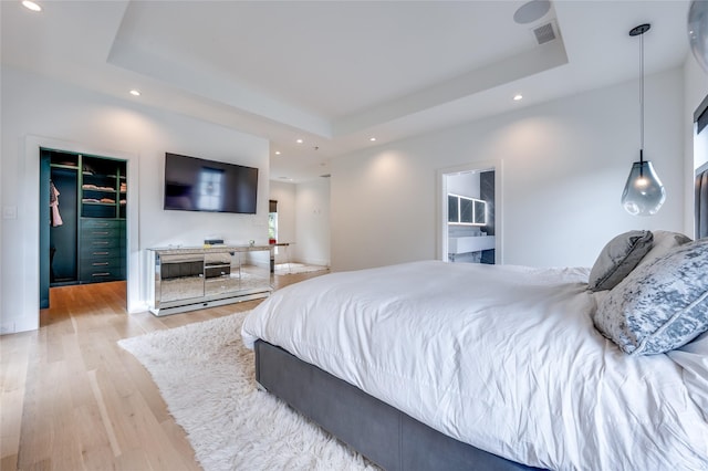 bedroom featuring a raised ceiling, a walk in closet, and light hardwood / wood-style floors