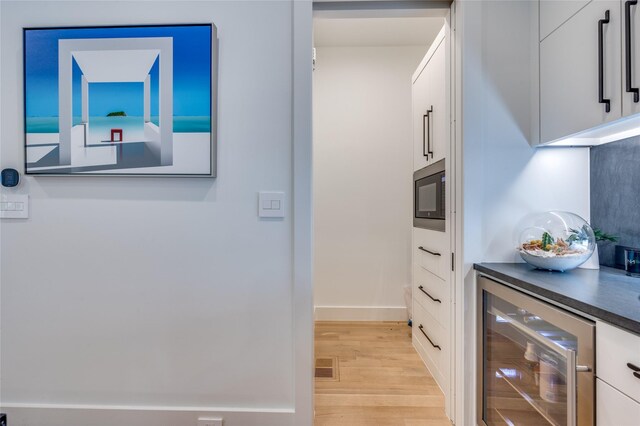 kitchen with light hardwood / wood-style flooring, white cabinetry, wine cooler, and black microwave