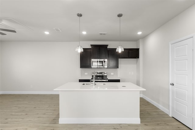 kitchen featuring ceiling fan, light hardwood / wood-style floors, a center island with sink, pendant lighting, and appliances with stainless steel finishes