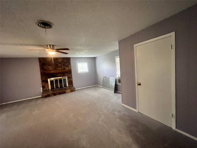 unfurnished living room with light carpet, a textured ceiling, a stone fireplace, and ceiling fan