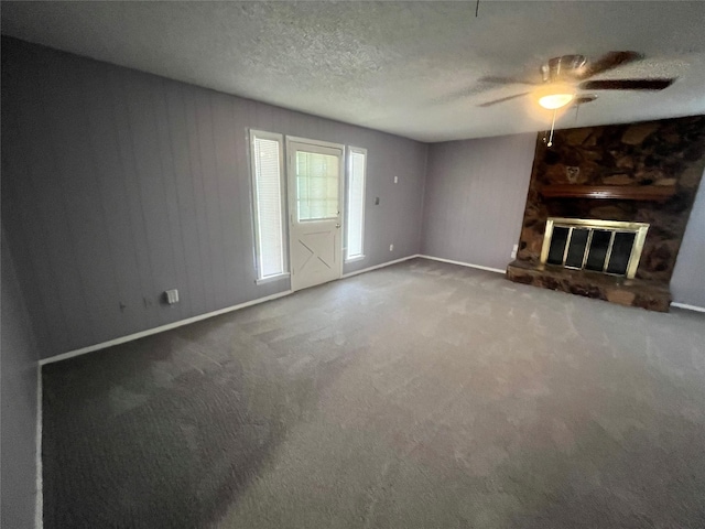 unfurnished living room with ceiling fan, a stone fireplace, wood walls, carpet floors, and a textured ceiling