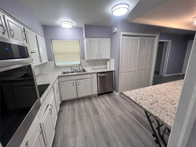 kitchen featuring light stone counters, stainless steel appliances, sink, light hardwood / wood-style flooring, and white cabinetry