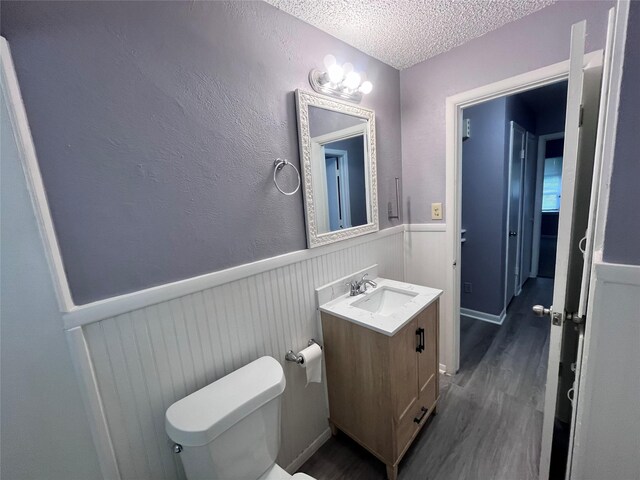 bathroom with an inviting chandelier, wood-type flooring, a textured ceiling, toilet, and vanity