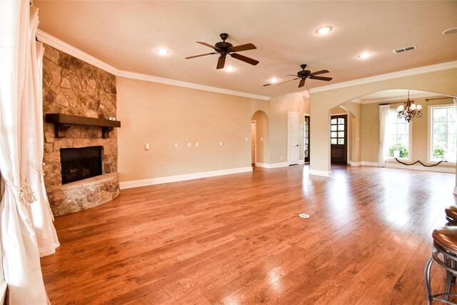 unfurnished living room featuring hardwood / wood-style floors, ceiling fan with notable chandelier, a stone fireplace, and crown molding