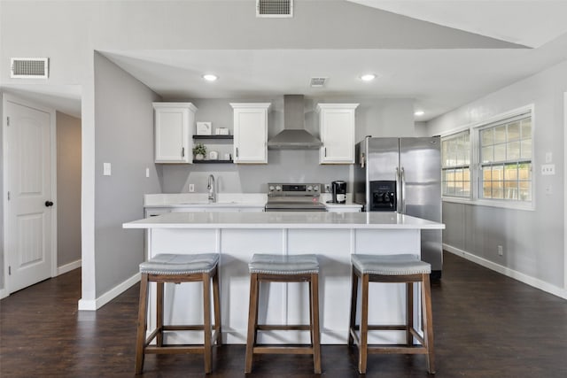 kitchen with a breakfast bar area, white cabinets, stainless steel appliances, and wall chimney range hood