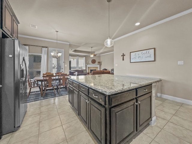 kitchen featuring ceiling fan, light stone counters, stainless steel fridge, dark brown cabinets, and a kitchen island