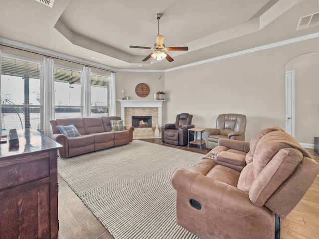 living room featuring ceiling fan, crown molding, a tray ceiling, a fireplace, and light wood-type flooring