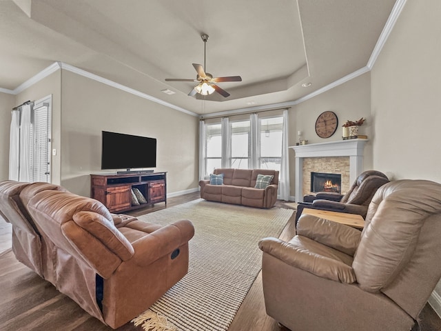 living room with ornamental molding, a raised ceiling, ceiling fan, hardwood / wood-style flooring, and a fireplace