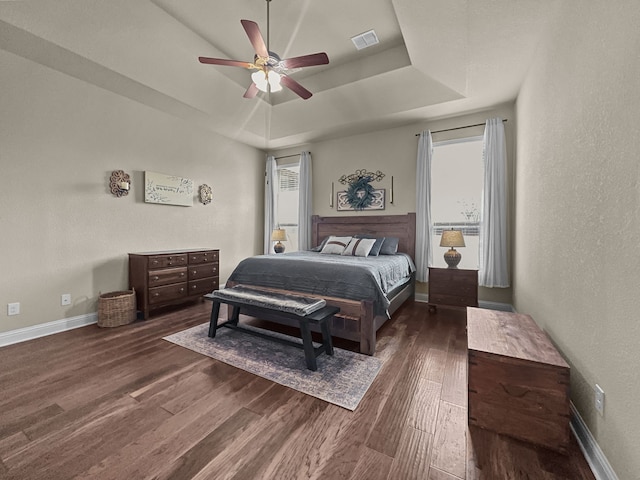 bedroom with a raised ceiling, ceiling fan, and dark hardwood / wood-style flooring