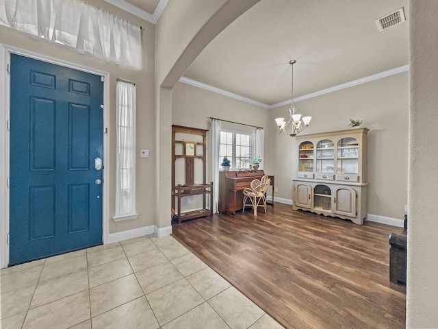 foyer entrance with light tile patterned floors, an inviting chandelier, and crown molding