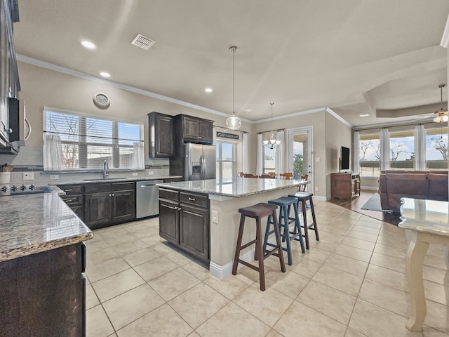 kitchen featuring a center island, stainless steel appliances, light stone counters, decorative light fixtures, and a breakfast bar area