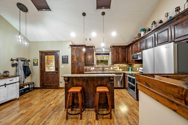 kitchen with stainless steel appliances, a kitchen breakfast bar, backsplash, pendant lighting, and a kitchen island