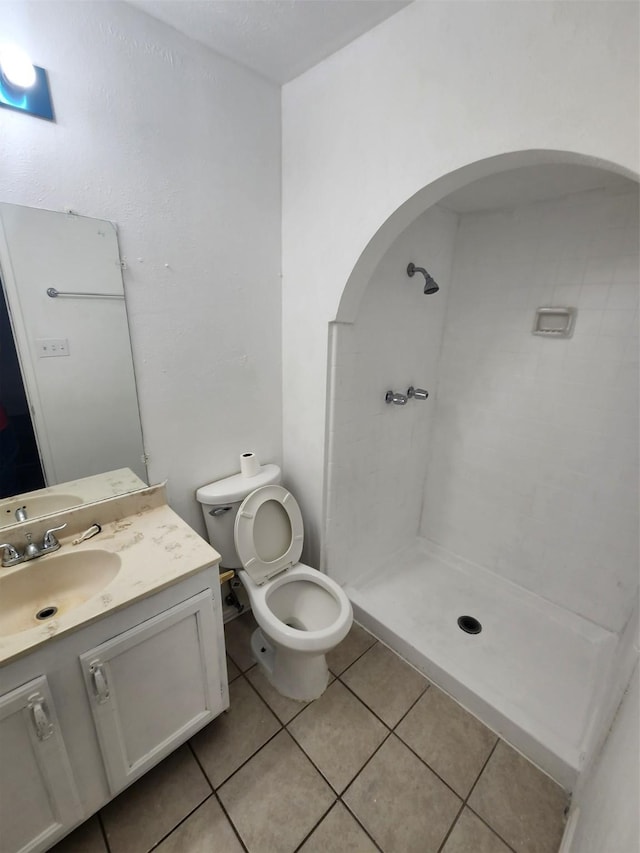 bathroom with a tile shower, tile patterned flooring, vanity, and toilet