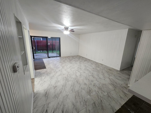 unfurnished living room featuring ceiling fan and wood walls