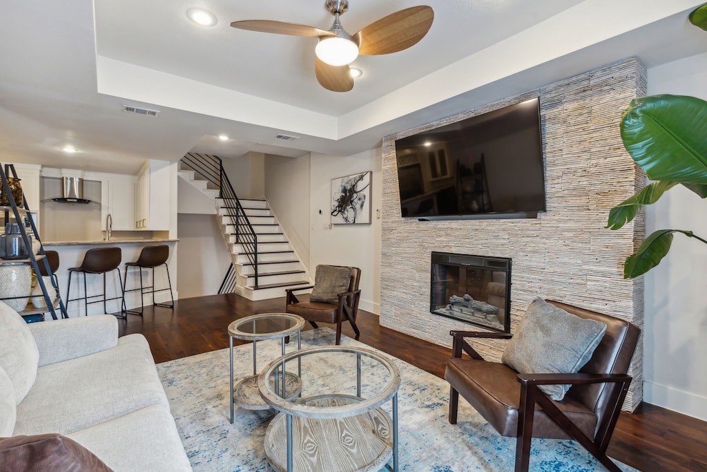 living room featuring a tray ceiling, ceiling fan, a fireplace, and dark hardwood / wood-style floors