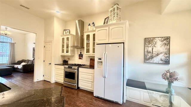 kitchen featuring stainless steel range with gas cooktop, dark hardwood / wood-style flooring, white fridge with ice dispenser, wall chimney range hood, and white cabinets