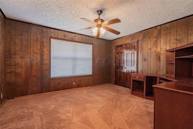 unfurnished office with light carpet, wood walls, ceiling fan, and a textured ceiling