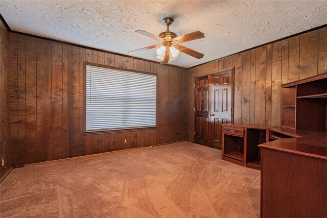 unfurnished office featuring ceiling fan, carpet flooring, a textured ceiling, and wood walls