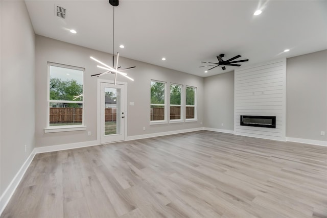 unfurnished living room with ceiling fan with notable chandelier, a large fireplace, and light hardwood / wood-style flooring