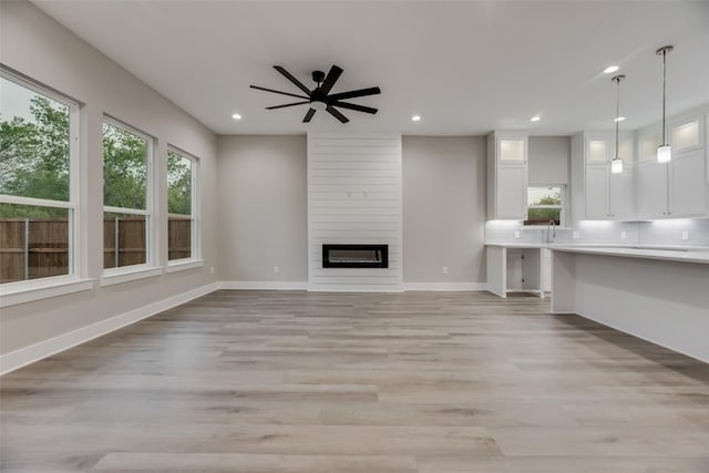 unfurnished living room featuring ceiling fan, a fireplace, light hardwood / wood-style floors, and sink