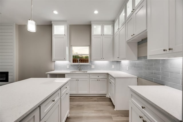 kitchen featuring light stone counters, sink, white cabinets, and hanging light fixtures