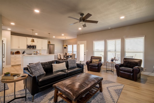 living room with ceiling fan, light hardwood / wood-style flooring, and a textured ceiling