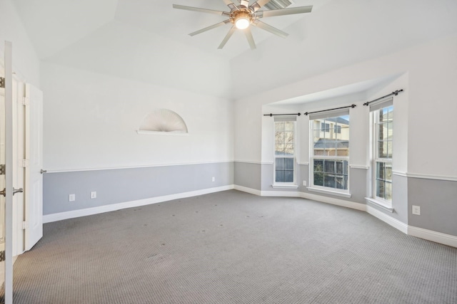 carpeted spare room with vaulted ceiling, a raised ceiling, and ceiling fan