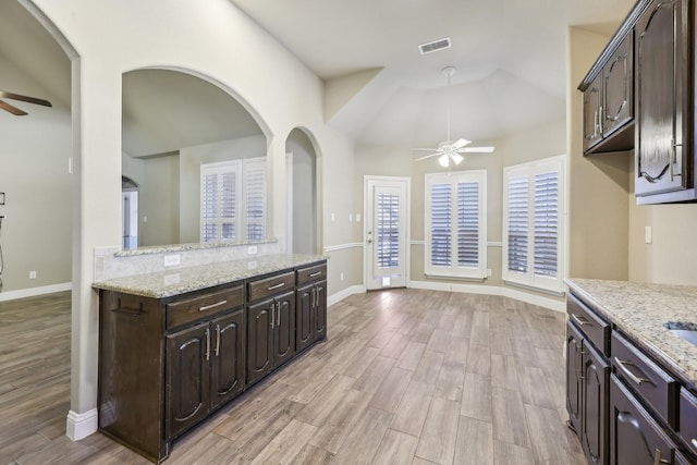 kitchen with light stone counters, dark brown cabinets, ceiling fan, and light hardwood / wood-style flooring