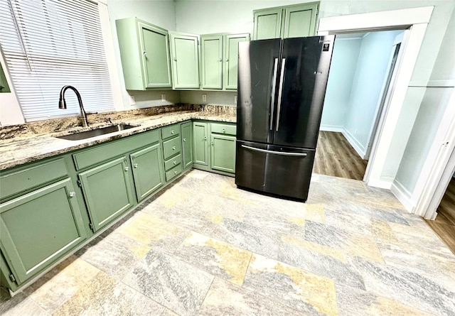 kitchen with fridge, green cabinetry, light stone countertops, and sink