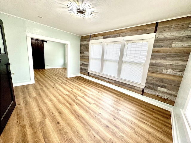 empty room featuring crown molding, wood walls, a textured ceiling, and light wood-type flooring