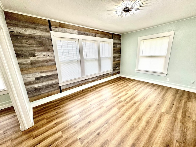 unfurnished room featuring wood walls, plenty of natural light, light hardwood / wood-style flooring, and a textured ceiling