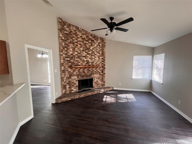 unfurnished living room featuring ceiling fan with notable chandelier, dark hardwood / wood-style flooring, lofted ceiling, and a brick fireplace