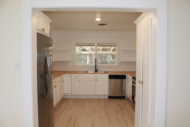 kitchen with butcher block countertops, sink, white cabinets, light hardwood / wood-style floors, and stainless steel appliances