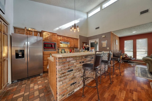 kitchen featuring stainless steel refrigerator with ice dispenser, a kitchen breakfast bar, built in microwave, a high ceiling, and hanging light fixtures