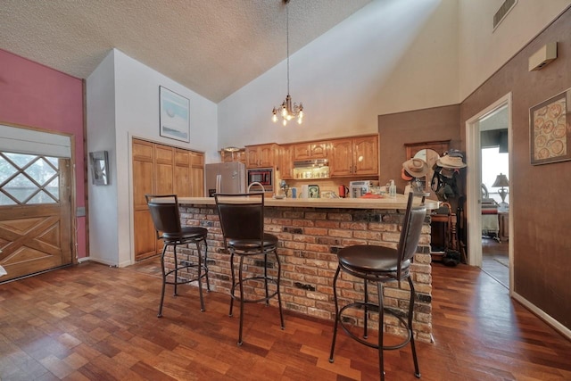 kitchen featuring stainless steel fridge, wood-type flooring, high vaulted ceiling, an inviting chandelier, and a breakfast bar area