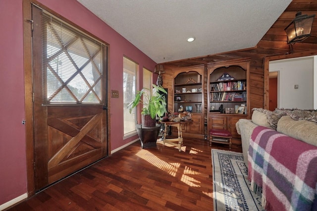 entrance foyer with lofted ceiling, wooden walls, dark hardwood / wood-style flooring, and a textured ceiling