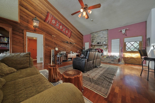 living room with hardwood / wood-style floors, wooden walls, vaulted ceiling, ceiling fan, and a textured ceiling