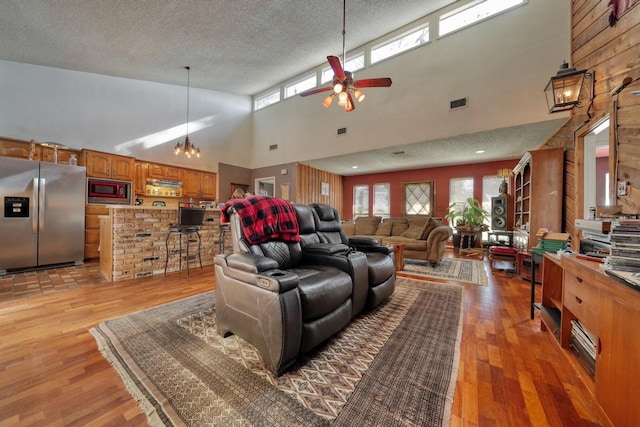 living room featuring a high ceiling, ceiling fan with notable chandelier, light hardwood / wood-style floors, and plenty of natural light