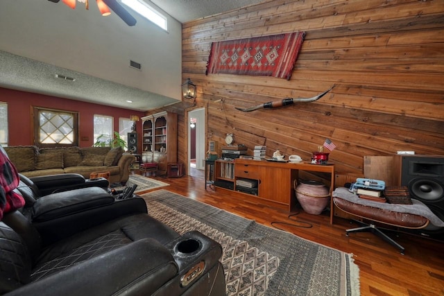 living room with ceiling fan, wood walls, wood-type flooring, and a textured ceiling