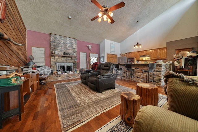 living room with a brick fireplace, high vaulted ceiling, wood-type flooring, a textured ceiling, and ceiling fan with notable chandelier