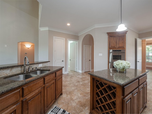 kitchen with double oven, crown molding, sink, dark stone countertops, and a kitchen island