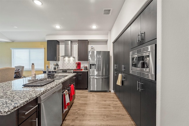 kitchen featuring sink, wall chimney exhaust hood, tasteful backsplash, light hardwood / wood-style floors, and stainless steel appliances