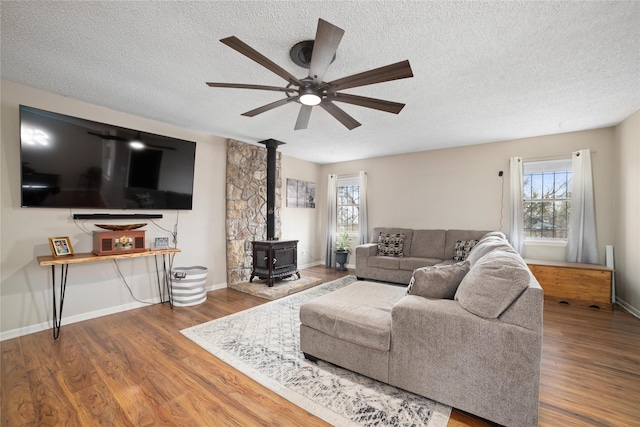 living room with ceiling fan, wood-type flooring, a textured ceiling, and a wood stove