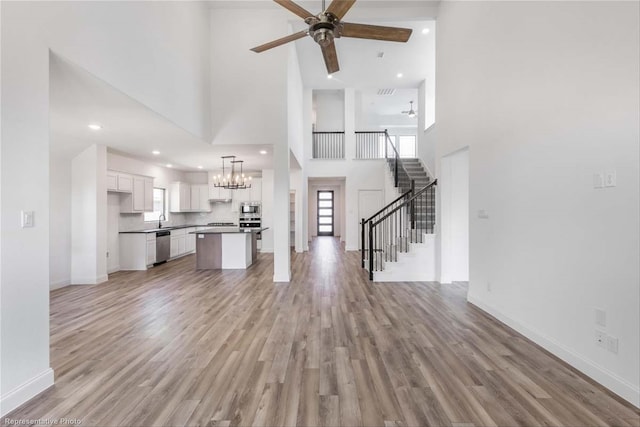 unfurnished living room with a high ceiling, sink, ceiling fan with notable chandelier, and light hardwood / wood-style floors