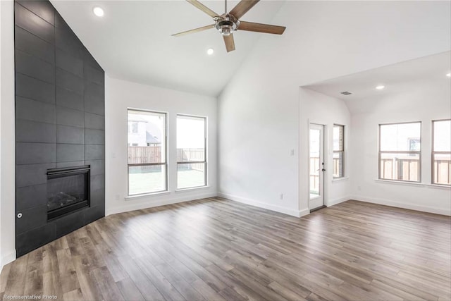 unfurnished living room with ceiling fan, light hardwood / wood-style floors, high vaulted ceiling, and a tiled fireplace