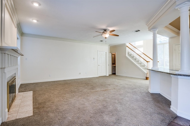 unfurnished living room featuring a tile fireplace, ceiling fan, ornamental molding, ornate columns, and light colored carpet