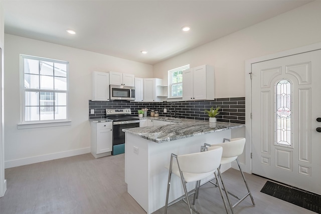 kitchen with white cabinets, a kitchen breakfast bar, light stone countertops, kitchen peninsula, and stainless steel appliances